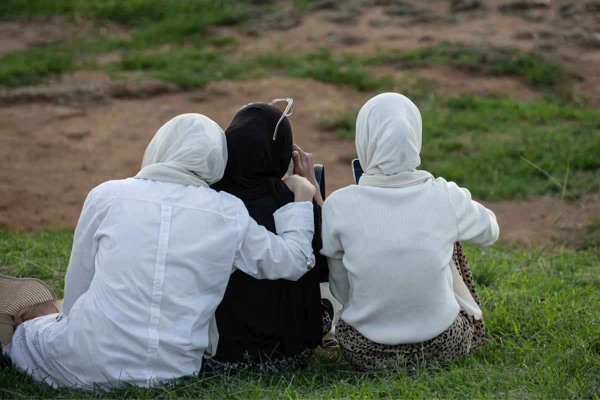 Three Muslim sisters in hijabs sitting together, viewed from behind so no faces are visible